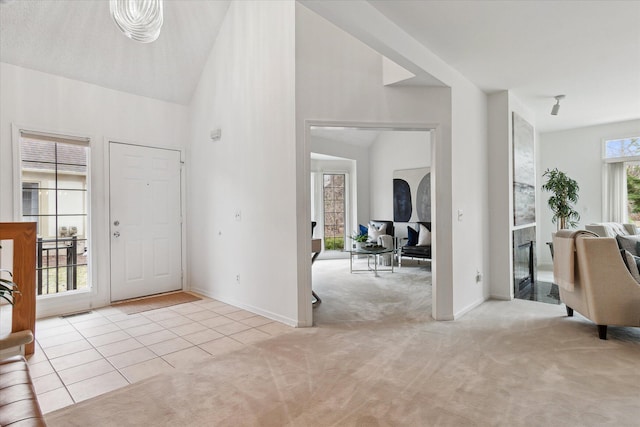tiled entrance foyer featuring baseboards, high vaulted ceiling, and carpet