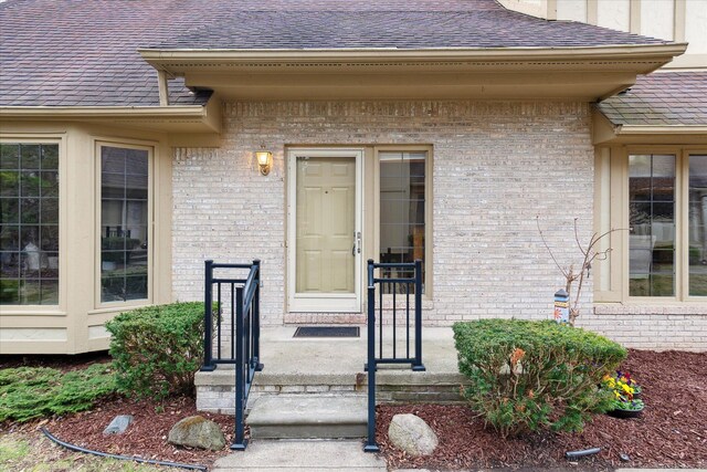 entrance to property featuring a shingled roof and brick siding