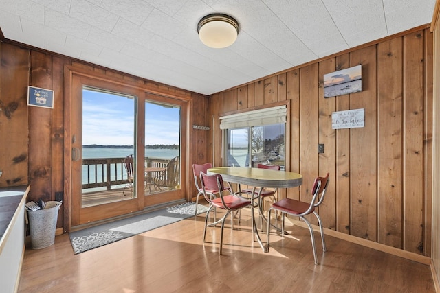 dining room featuring a water view, wood finished floors, and wood walls