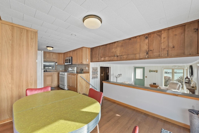 kitchen with stainless steel microwave, baseboards, decorative backsplash, white range with gas stovetop, and wood finished floors