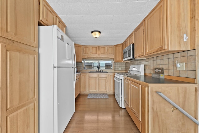 kitchen with tasteful backsplash, white appliances, light brown cabinetry, a sink, and wood finished floors