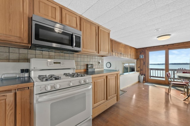 kitchen with stainless steel microwave, dark countertops, wood finished floors, tasteful backsplash, and white gas range oven