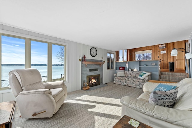 carpeted living area with a fireplace, a water view, and wood walls
