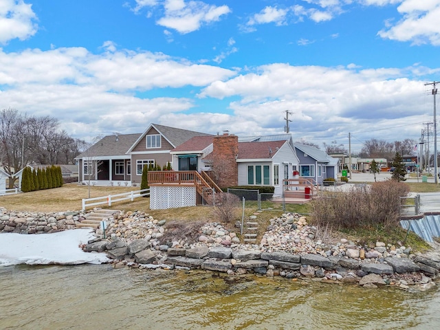 rear view of property with a deck with water view, fence, a chimney, and a sunroom