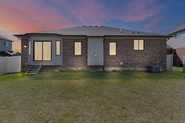 back of property at dusk with fence, central AC unit, a lawn, and brick siding