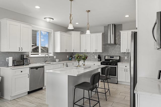 kitchen featuring a breakfast bar, wall chimney exhaust hood, white cabinets, a sink, and stainless steel appliances