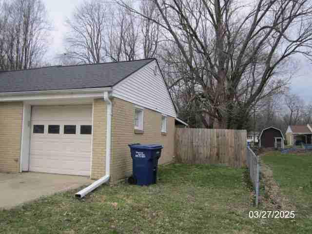 view of side of property featuring brick siding, concrete driveway, a garage, and fence