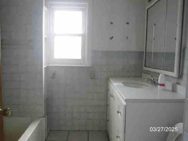 full bath with tile walls, tile patterned flooring, and vanity