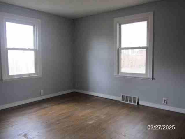 empty room featuring wood finished floors, baseboards, and visible vents