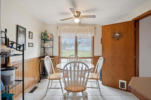 dining area with a wainscoted wall, ceiling fan, wooden walls, and light tile patterned floors