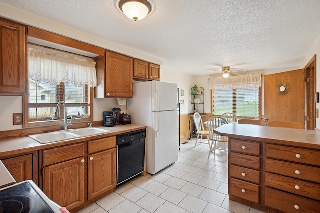 kitchen with light countertops, a sink, freestanding refrigerator, dishwasher, and brown cabinetry