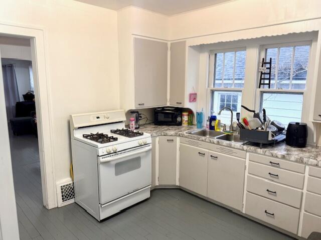 1024 Madison St, Muskegon, MI 49442 - kitchen with white cabinetry, light countertops, a sink, white gas range oven, and wood finished floors