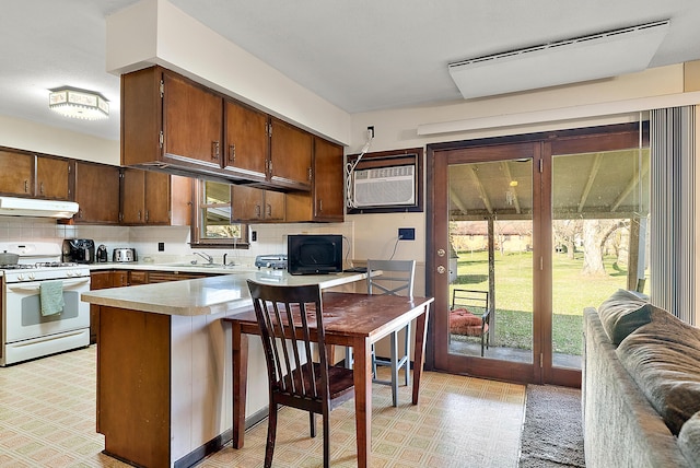 kitchen featuring light countertops, white gas range, a peninsula, under cabinet range hood, and an AC wall unit