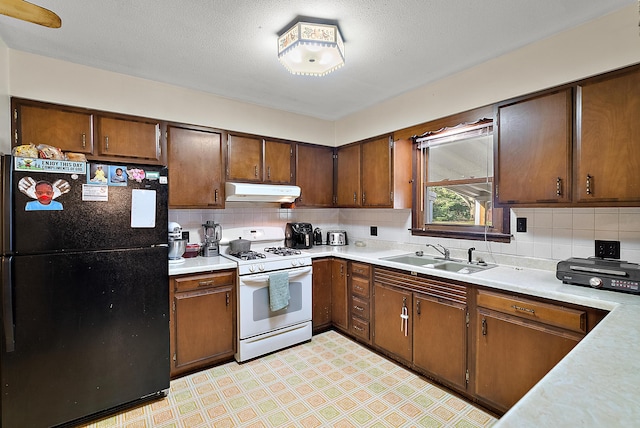 kitchen with a sink, freestanding refrigerator, gas range gas stove, light floors, and under cabinet range hood