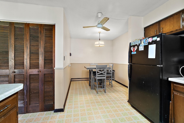 kitchen with freestanding refrigerator, a ceiling fan, light countertops, and a wainscoted wall