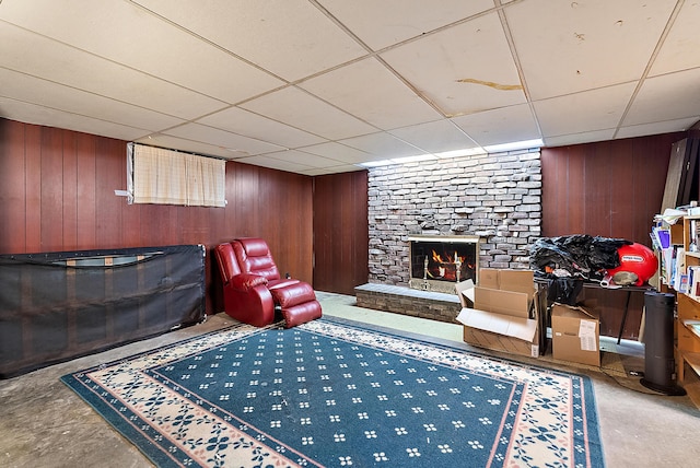 living area with a drop ceiling, a brick fireplace, concrete floors, and wooden walls