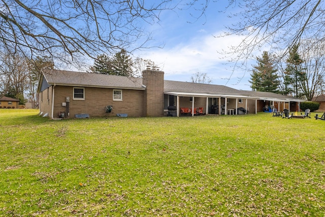 back of property featuring an attached carport, a chimney, brick siding, and a yard