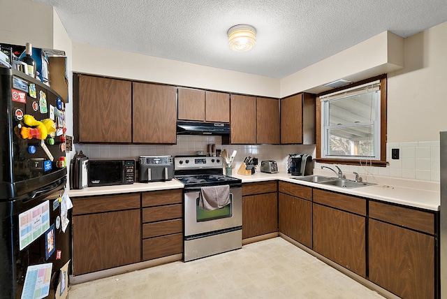 kitchen featuring light countertops, a sink, freestanding refrigerator, under cabinet range hood, and stainless steel electric range oven