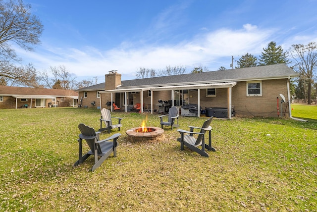 rear view of house with a chimney, brick siding, a hot tub, a fire pit, and a yard