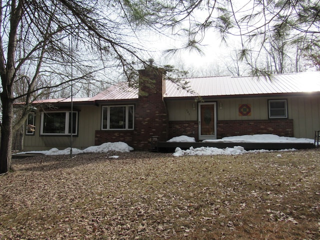 view of front of home featuring brick siding, a chimney, and metal roof