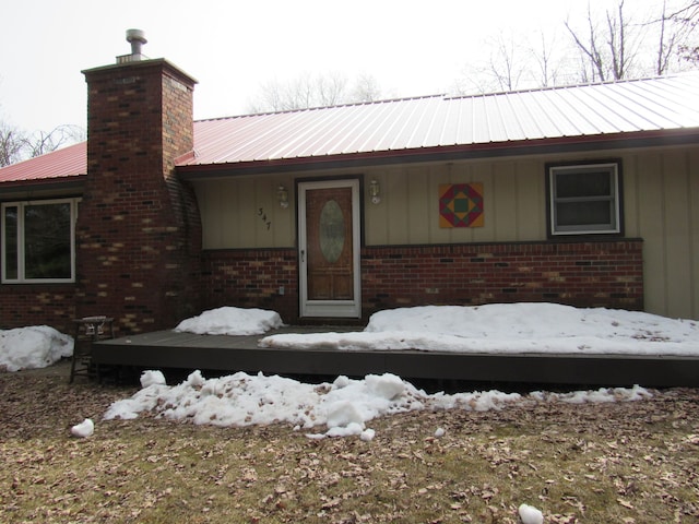 snow covered property entrance featuring board and batten siding, brick siding, and a chimney