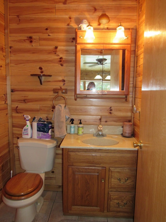 bathroom with toilet, vanity, wood walls, and tile patterned flooring