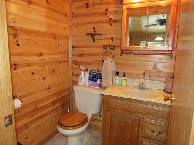 half bath with tile patterned floors, wooden walls, toilet, and vanity