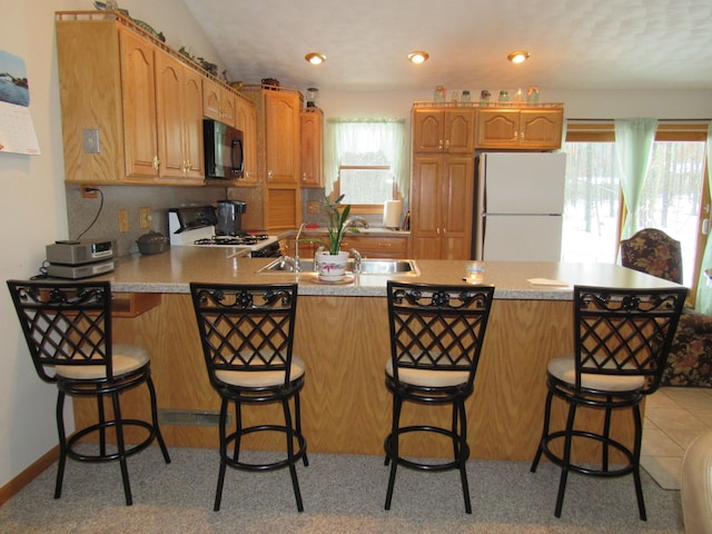 kitchen with white appliances, light countertops, a breakfast bar, and a peninsula