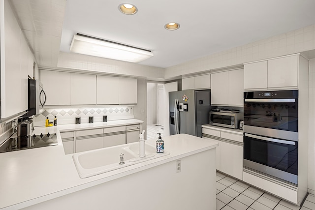 kitchen featuring light countertops, backsplash, a peninsula, and appliances with stainless steel finishes