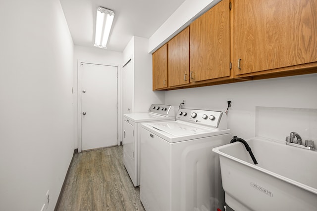 laundry area with independent washer and dryer, light wood-style floors, cabinet space, and a sink
