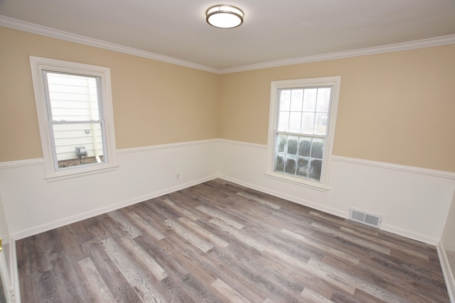 spare room featuring wood finished floors, ornamental molding, baseboards, and visible vents