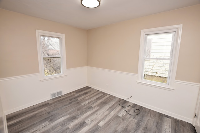 spare room with a wealth of natural light, visible vents, baseboards, and dark wood-style flooring