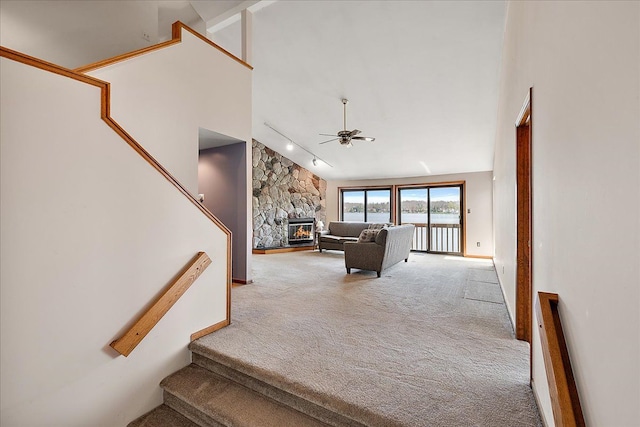 stairway featuring rail lighting, a ceiling fan, carpet floors, and a fireplace
