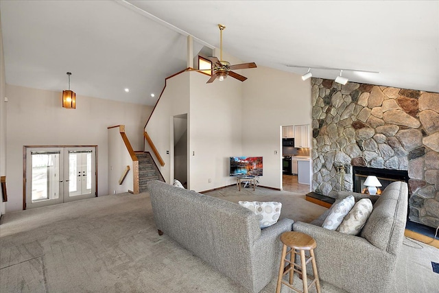 living area featuring carpet floors, stairway, a stone fireplace, high vaulted ceiling, and a ceiling fan