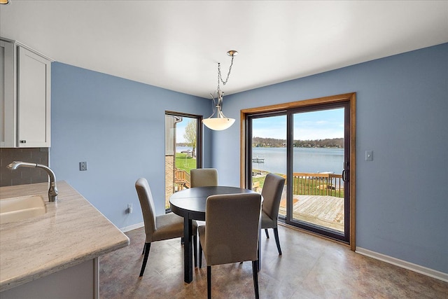dining space featuring concrete flooring, a water view, and baseboards