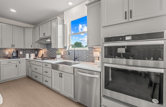 16104 Conifer Ln, Clinton Township, MI 48038 - kitchen with appliances with stainless steel finishes, light countertops, under cabinet range hood, light wood-type flooring, and backsplash