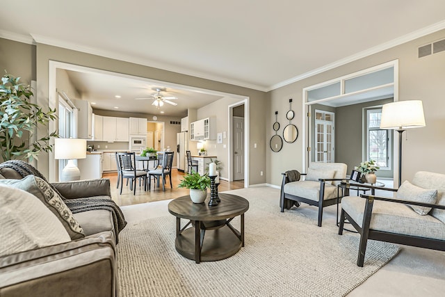 living area featuring baseboards, visible vents, ornamental molding, and a ceiling fan