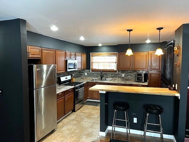 kitchen featuring a kitchen bar, wooden counters, a sink, a peninsula, and appliances with stainless steel finishes