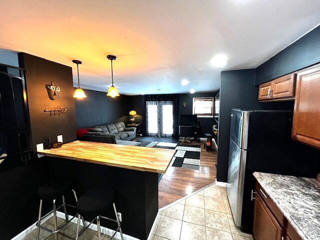 kitchen featuring light tile patterned flooring, wood counters, open floor plan, a kitchen breakfast bar, and freestanding refrigerator
