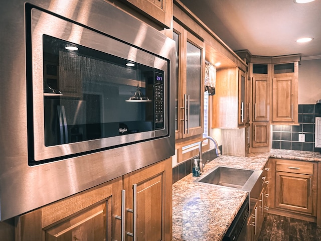 kitchen with brown cabinetry, decorative backsplash, stainless steel microwave, and light stone counters