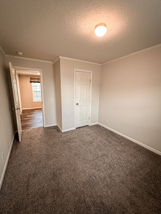 spare room featuring ornamental molding, baseboards, dark colored carpet, and a textured ceiling