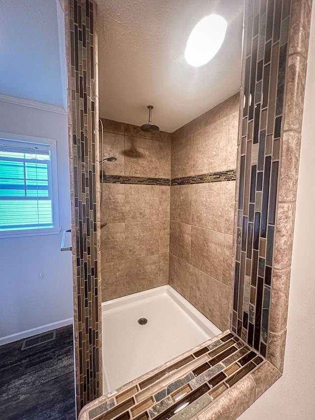 full bath with tiled shower, visible vents, and baseboards