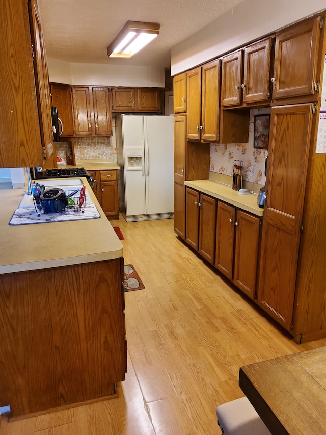 2415 Needham St, Saginaw, MI 48601 - kitchen featuring brown cabinetry, light wood-style flooring, stainless steel microwave, and white refrigerator with ice dispenser