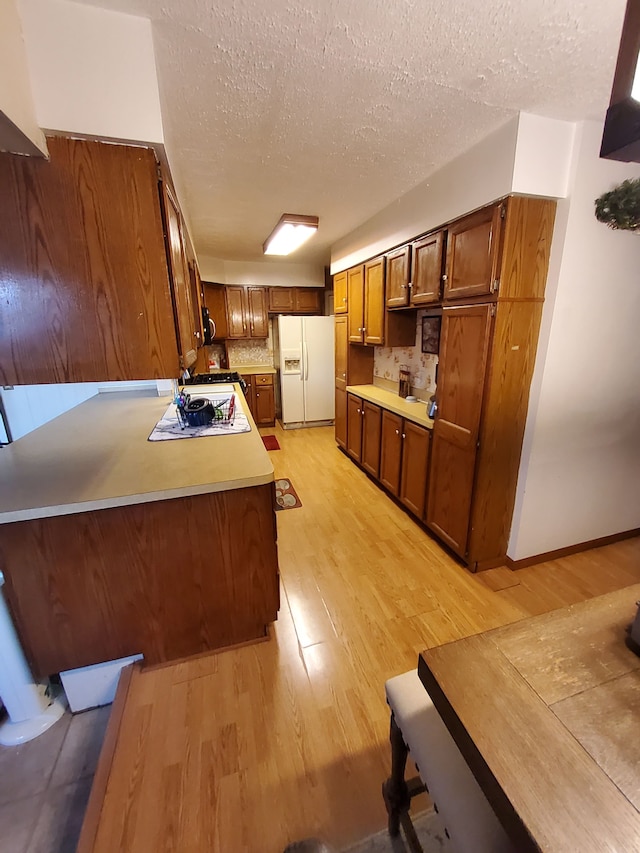 2415 Needham St, Saginaw, MI 48601 - kitchen with light countertops, white refrigerator with ice dispenser, light wood-type flooring, brown cabinetry, and decorative backsplash