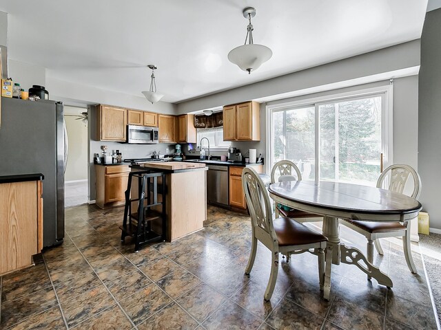 kitchen featuring stone finish floor, appliances with stainless steel finishes, hanging light fixtures, a center island, and a sink
