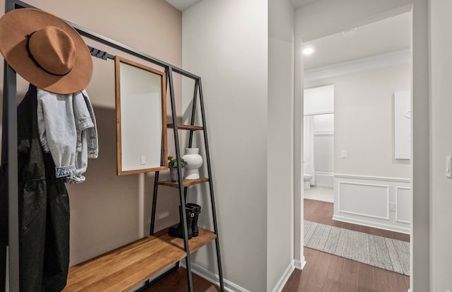 bathroom with a decorative wall, wood finished floors, crown molding, and wainscoting