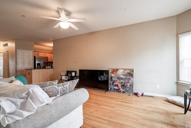 living area with visible vents, light wood-type flooring, a ceiling fan, and baseboards