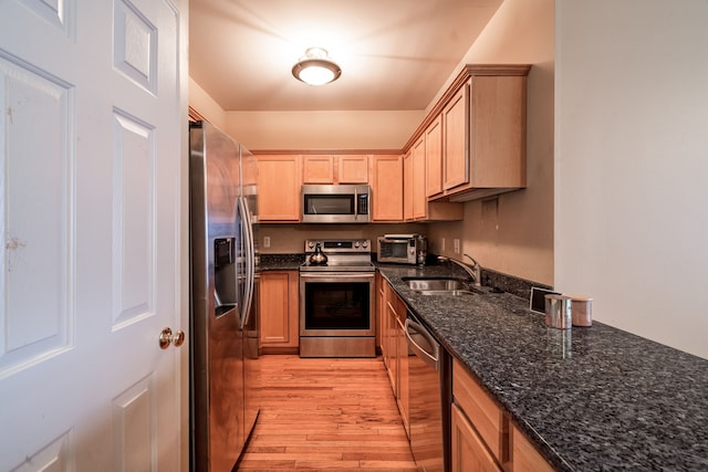 kitchen with dark stone countertops, a toaster, appliances with stainless steel finishes, a sink, and light wood-type flooring