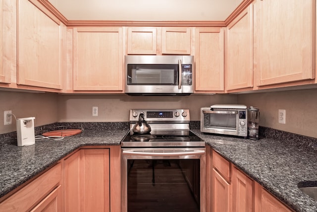 kitchen featuring dark stone counters, light brown cabinets, stainless steel appliances, and a toaster
