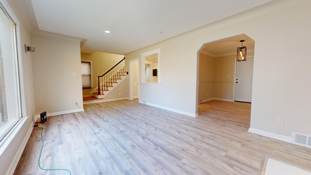empty room featuring light wood-type flooring, arched walkways, baseboards, and visible vents